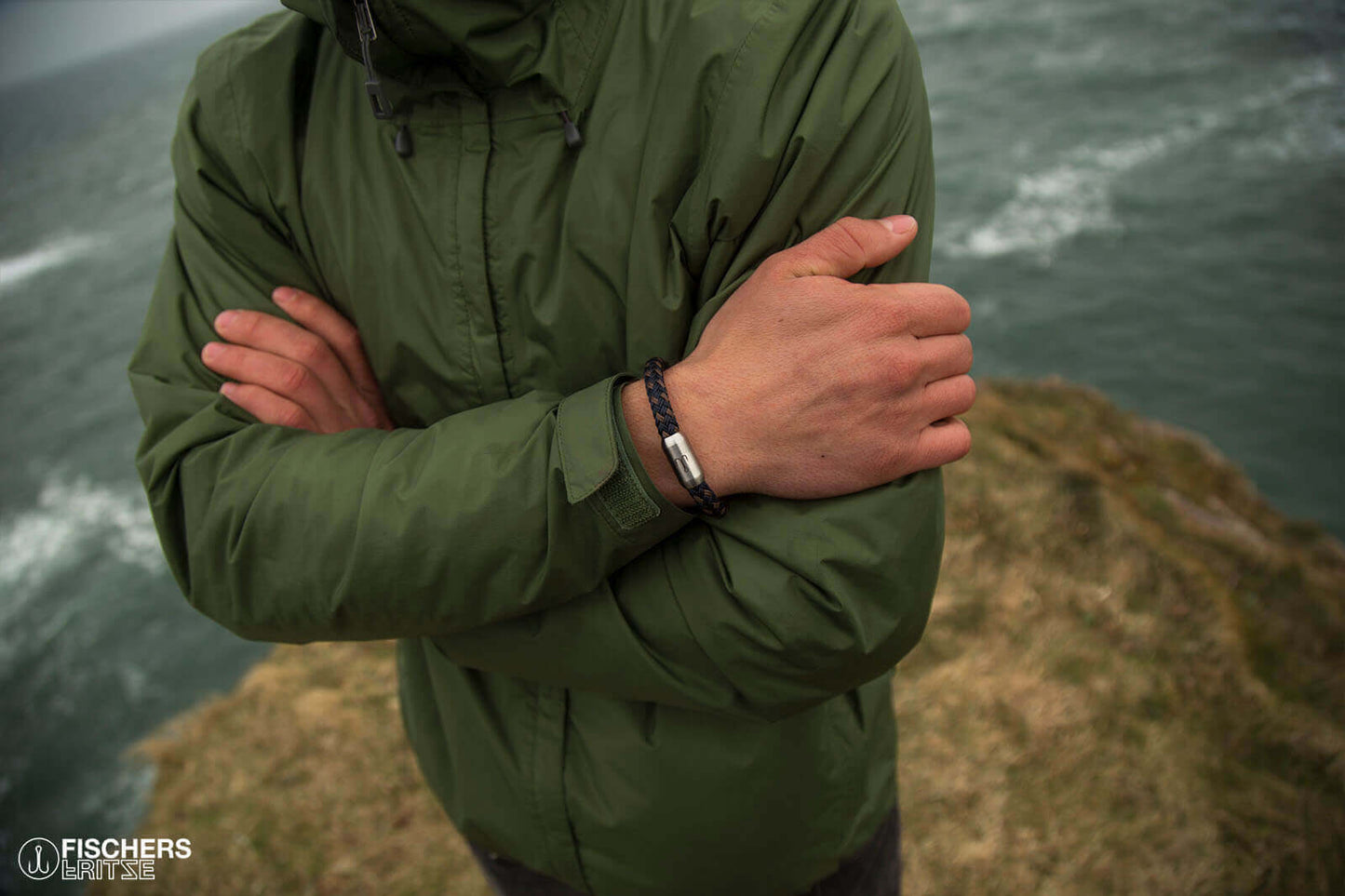 Mann steht auf Felsen an Kueste, trägt Armband marineblau braun mit Edelstahl Gravur von Fischers Fritze, aus Segeltau